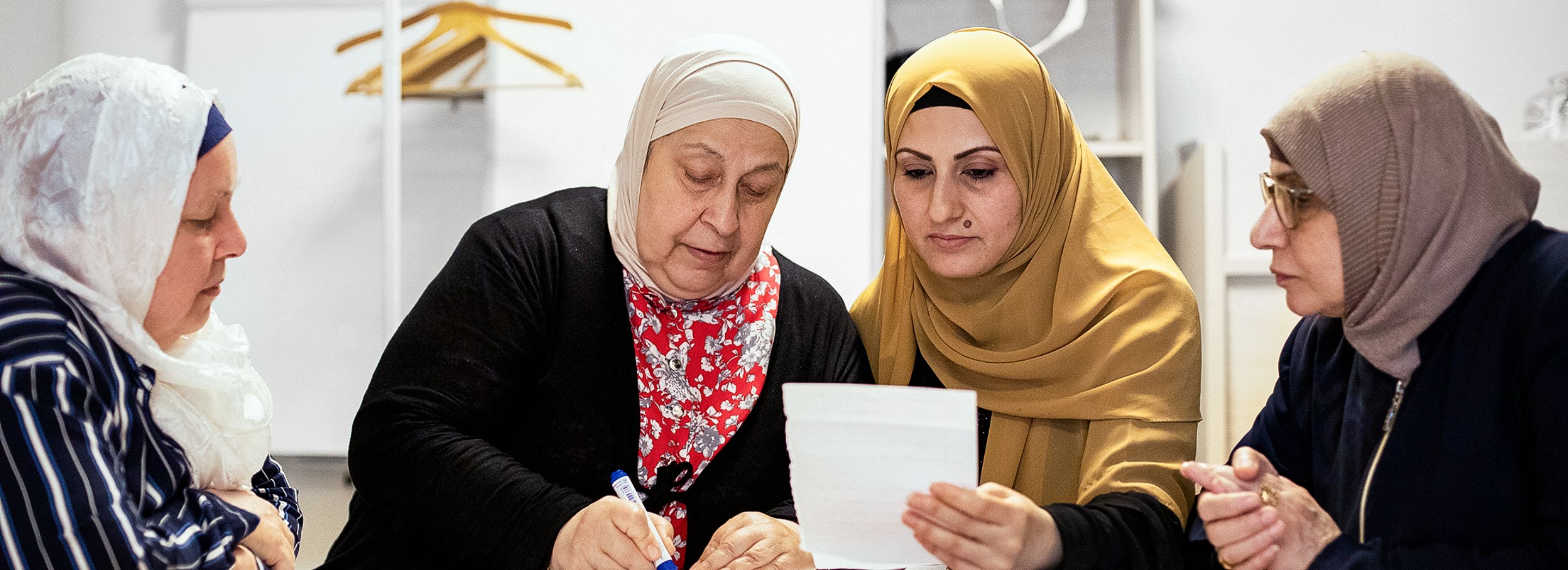 Foto: Vier Frauen mit Kopftüchern sitzen an einem Tisch und lernen gemeinsam.
