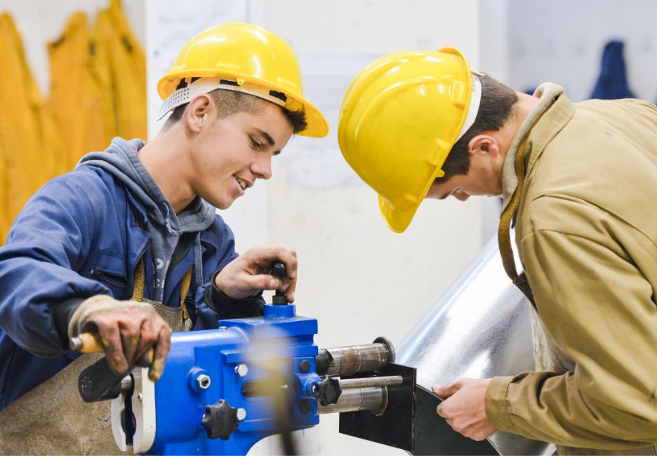 Foto: Zwei Männer mit Schutzhelmen arbeiten an einer Maschine. 